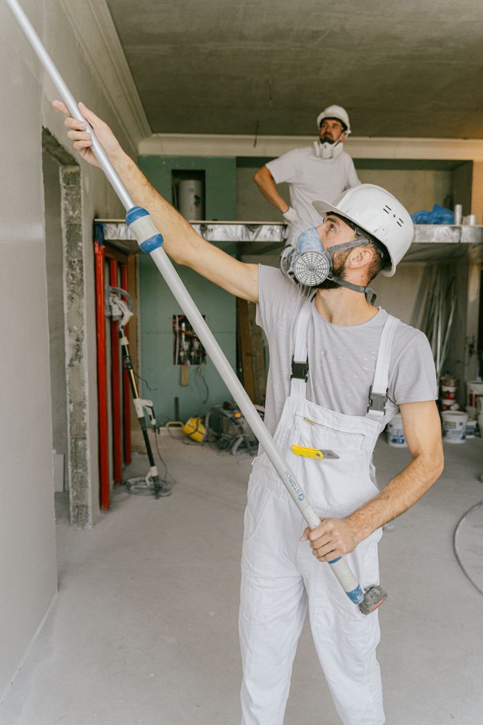 Home Two construction workers in safety gear are interior renovating, using a paint roller.